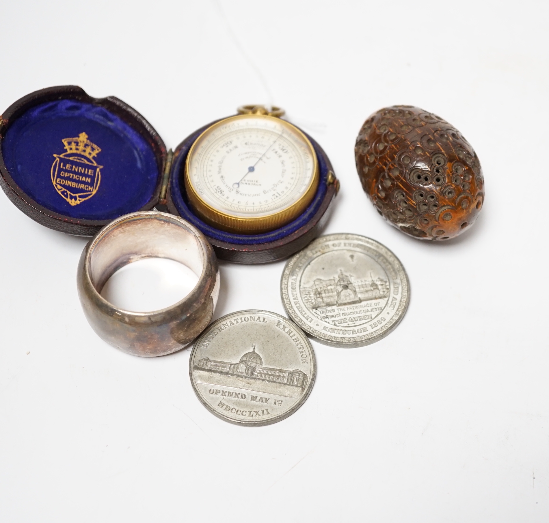 A Lennie brass pocket barometer, a carved coquilla nut, a silver plated napkin ring and two exhibition medallions